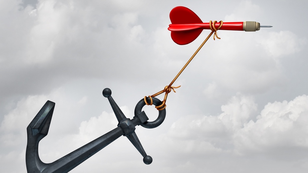 A dart with a heart-shaped tail is tied to a heavy anchor against a cloudy sky.