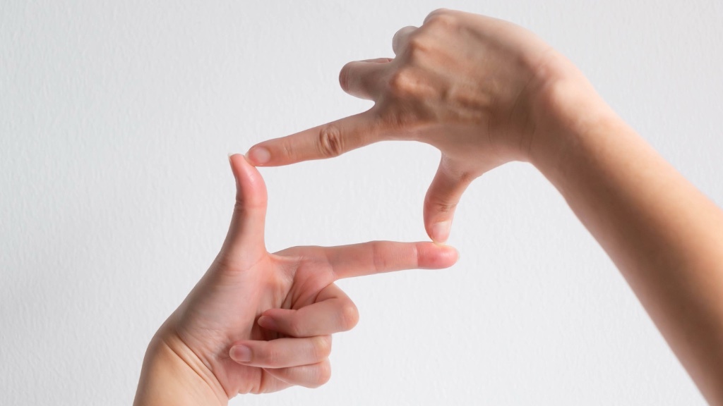 Two hands form a rectangular frame with their fingers against a plain white background, as if visualizing a picture or perspective.