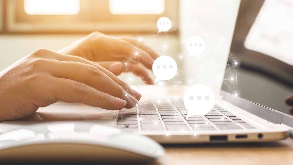 En person skriver på ett laptop-tangentbord medan digitala chattikoner svävar ovanför enheten.