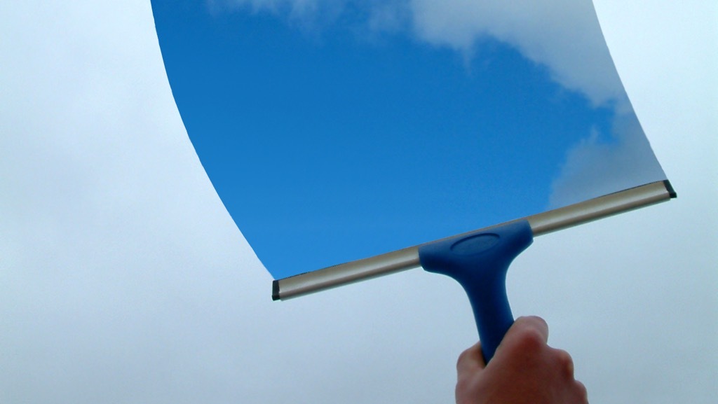 A hand is cleaning a window to the sky with a scraper.
