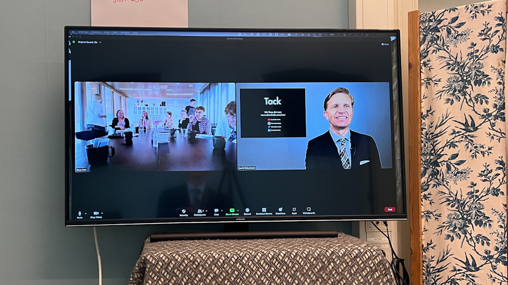 En storbilds-tv visande en Zoom-föreläsning där David Stiernholm föreläser till höger och deltagarna sitter till vänster