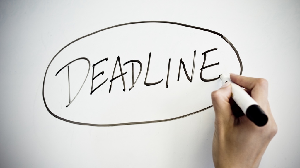 A hand is writing the word "Deadline" with a black pen on a whiteboard and then circle it.