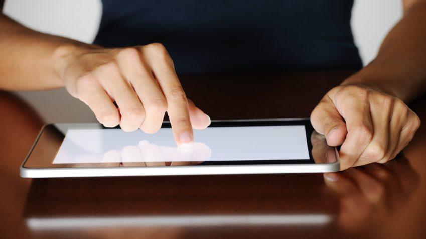 Person using a tablet wearing black clothes, keeping the tablet on a desk