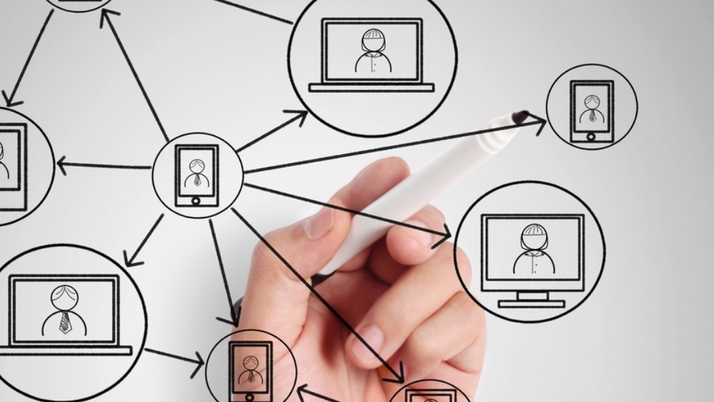 A hand is drawing a network diagram with interconnected icons of laptops and smartphones, representing communication links.
