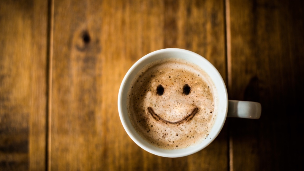 A cup of coffee with a smiley face drawn in the foam on a wooden table.