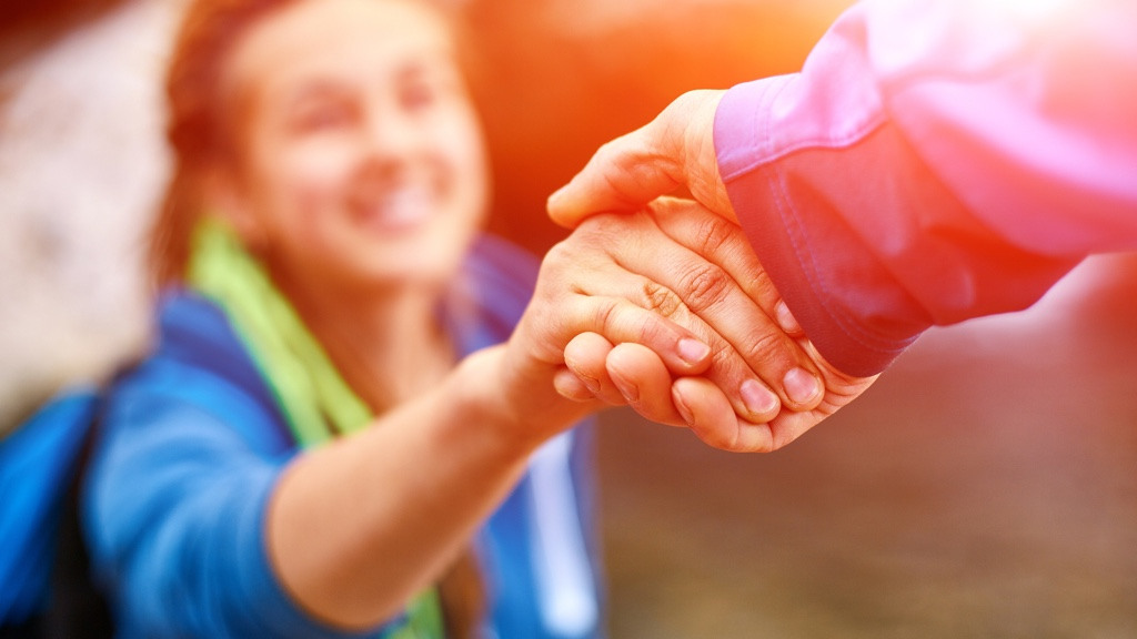 A person is helping another person up a slope by pulling them up by the hand.