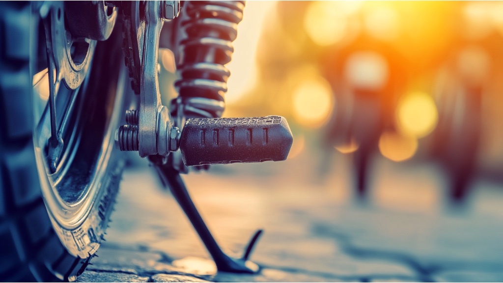 En närbild av en motorcykels kickstartspedal och fjädring med en oskarp solig bakgrund.