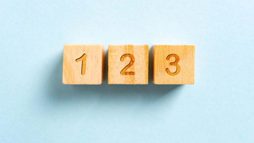 Three wooden blocks with the numbers 1, 2, and 3 engraved on them are lined up against a light blue background.
