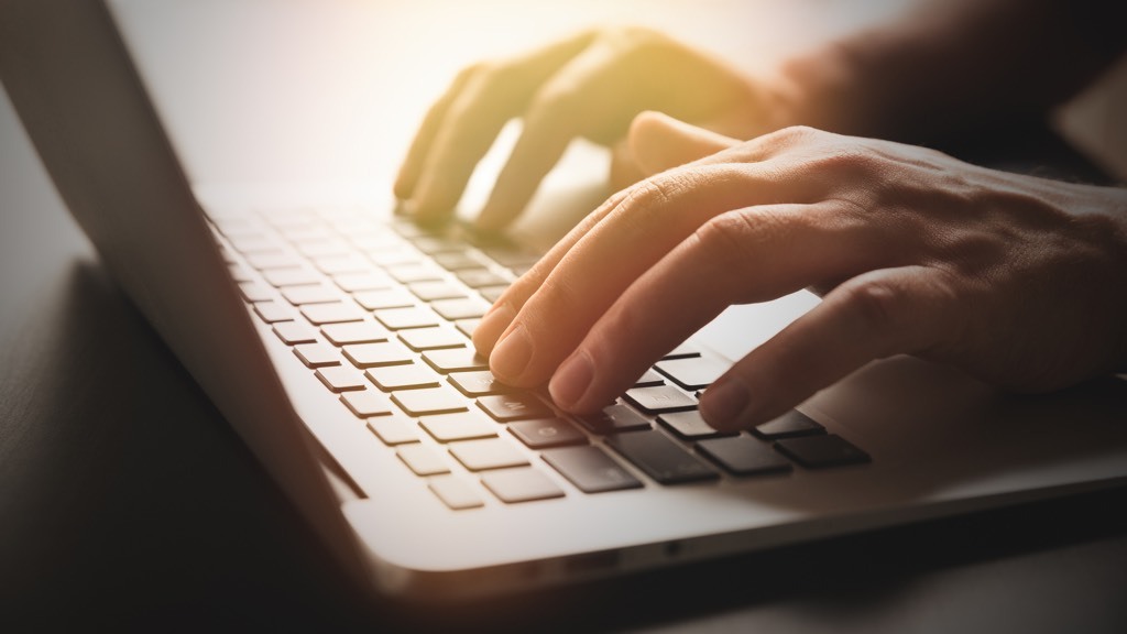 A person's hands are illuminated by a warm glow as they type on a laptop keyboard.