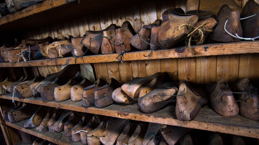 Wooden shoe lasts of various sizes are lined up on shelves in a workshop.