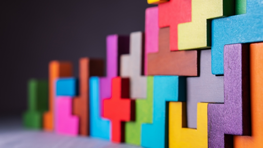 Colorful wooden puzzle pieces are interlocked in a complex, upright pattern against a dark background.