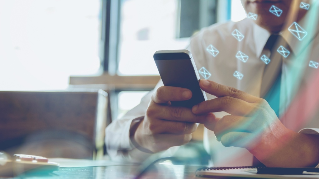 A man sits at a desk, reading a multitude of emails on his phone. Sunlight streams through the window, creating bokeh patterns. He is wearing a white shirt and a dark tie.