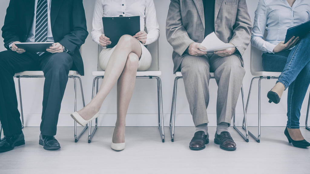 Four people are seated in a row with clipboards, preparing for an interview.