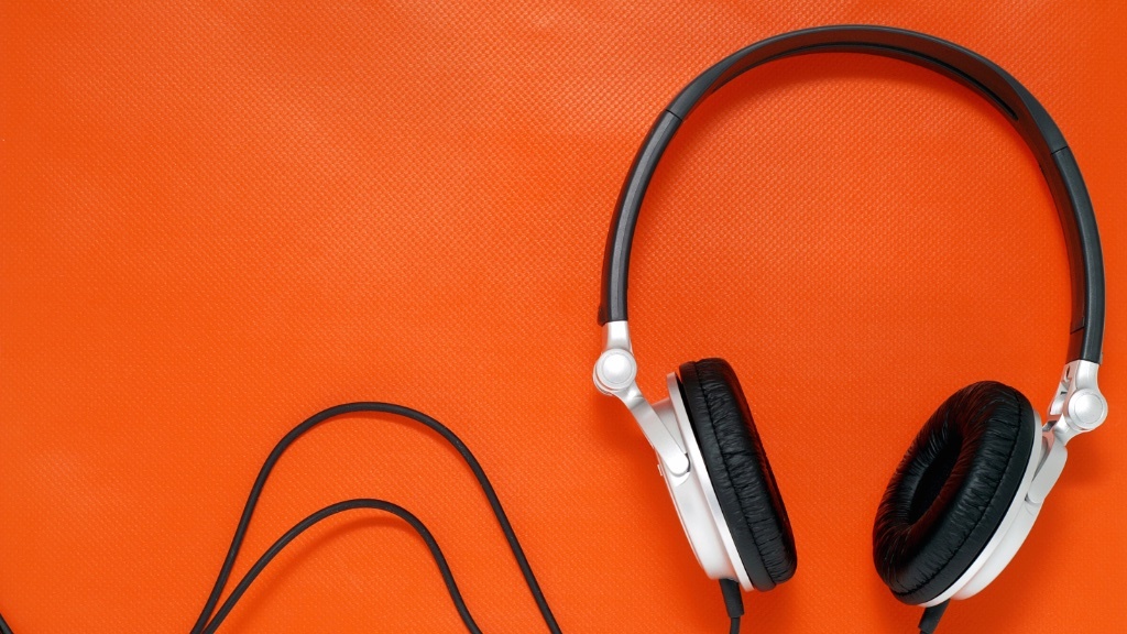 A pair of black and silver headphones with a black cord is lying on an orange textured surface.