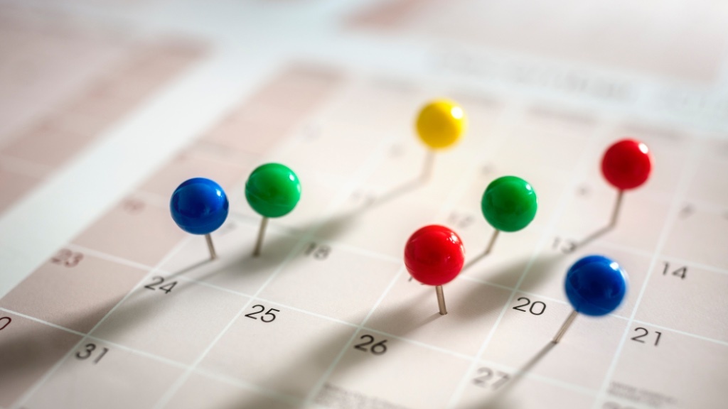 Flera färgglada nålar sitter fast i en kalender och markerar viktiga datum eller händelser.