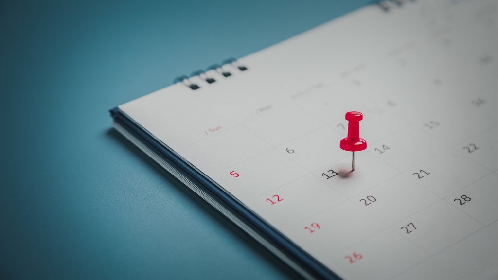 Red pin on a paper calendar on a blueish background.