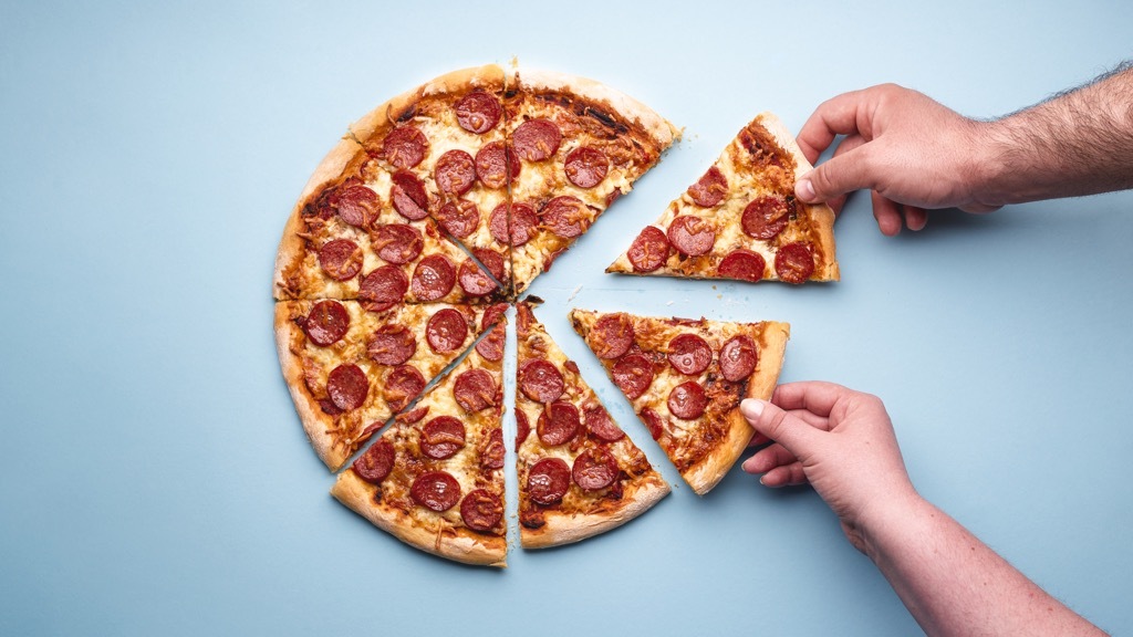 Två personer tar varsin bit pepperonipizza från en nästan hel pizza mot en blå bakgrund.