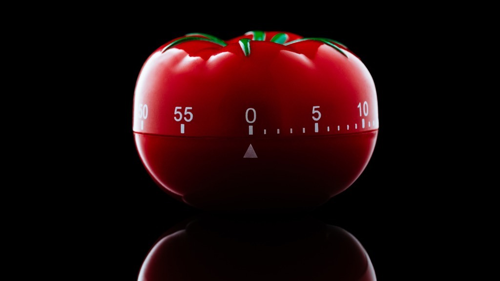Tomato shaped kitchen timer on a black, shiny counter top.