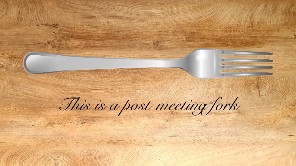 A metal fork lies on a wooden table above the text “This is a post-meeting fork,” written in elegant cursive.