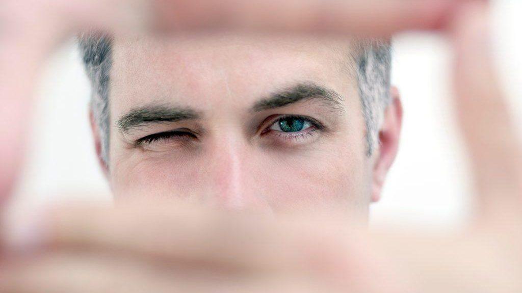 Man peeking with one eye through his hands