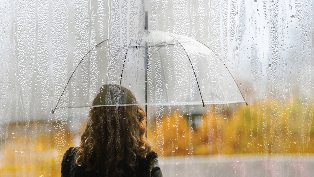 En kvinna står under ett transparent paraply i regn i höstmiljö.