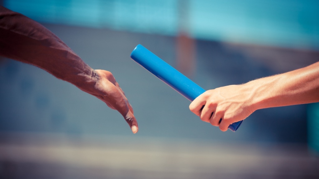 A baton is being handed over between two runners during a relay race.
