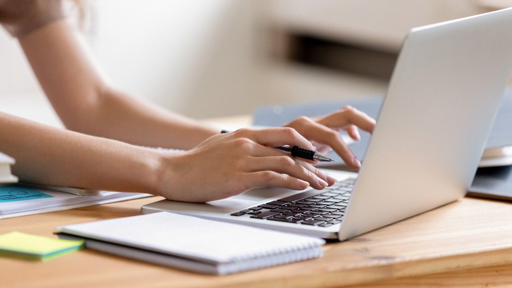 Two female hands typing on a laptop on a meeting table.