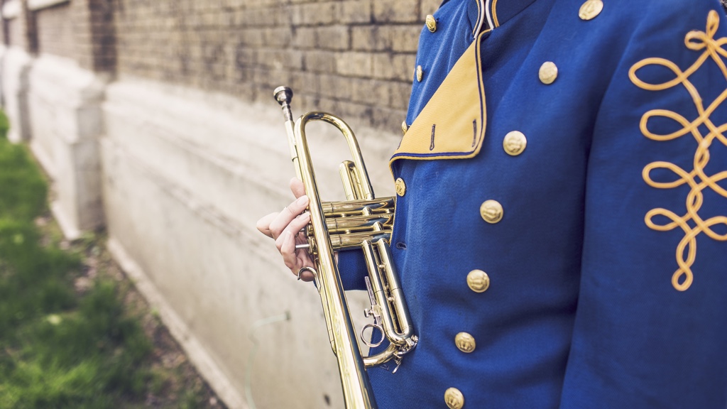 En person i en blå och guldig musikuniform håller en trumpet vid sin sida.