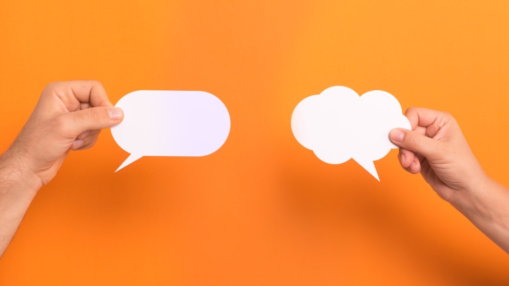 Two hands holding white, empty speech bubbles against an orange background.