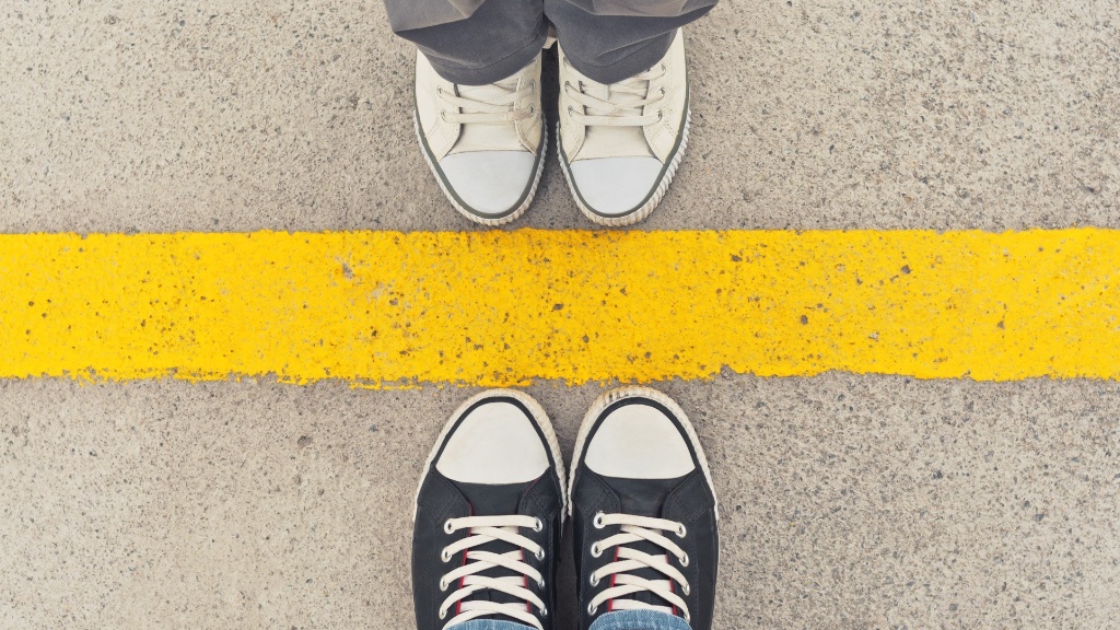 Two pairs of feet stand opposite each other on either side of a yellow line on the ground.