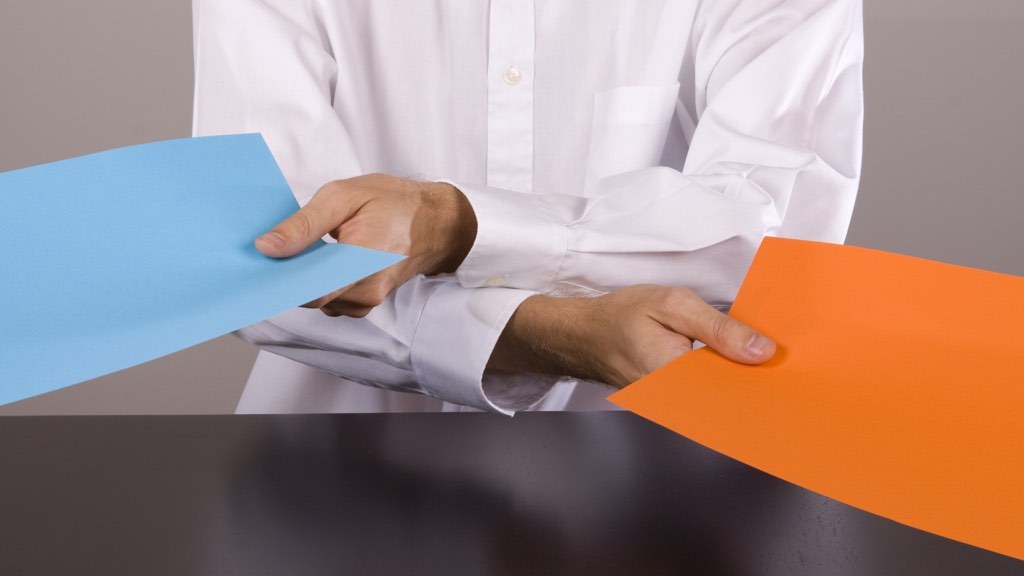 Two hands handing out a blue and an orange sheet of paper.