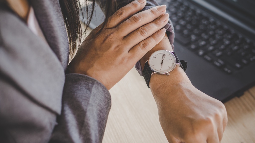 A person wearing a suit is checking the time on their wristwatch near a laptop.