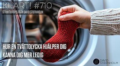 En hand i en vit stickad tröja håller i en röd stickad strumpa framför en öppen tvättmaskin.