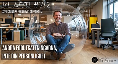 En leende man sitter med benen i kors i en genomskinlig bubbelstol mitt i ett modernt kontorslandskap.