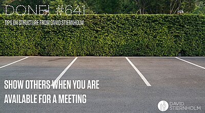 Several empty parking spaces are lined up in front of a tall, neatly trimmed hedge with trees in the background.