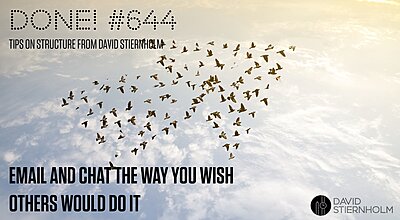 A large flock of birds flies together in a distinct arrow formation across a golden sky at sunrise or sunset.