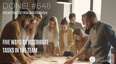 A group of eight people is gathered around a table in a modern office, intently discussing and dividing tasks using papers and small blocks, suggesting collaborative planning or project work.