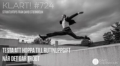 En man i kostym hoppar i luften mellan två betongstrukturer under en dramatisk, molntäckt himmel.