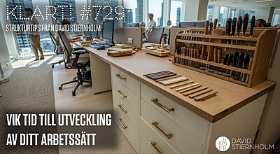 Ett modernt kontorslandskap visar en ovanlig arbetsstation med prydligt uppställda träverktyg och stämjärn bredvid vanliga skrivbord med datorer – en blandning av hantverk och kontorsmiljö.