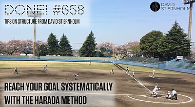 A youth baseball game is underway on a dirt field, with players in white uniforms and cherry blossom trees blooming in the background.