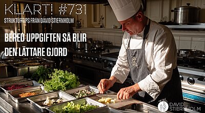 En kock i full mundering förbereder noggrant ingredienser vid en arbetsstation i ett professionellt kök, omgiven av prydligt organiserade brickor med färska råvaror och tillbehör.