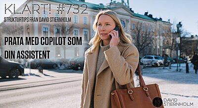 En kvinna i beige kappa promenerar genom en solig, vinterkall stadsgata och pratar i telefon, med en stor brun läderväska på axeln.