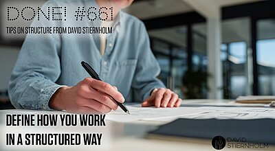 A person in a light denim shirt is sketching or writing on large sheets of paper at a bright, modern workspace.