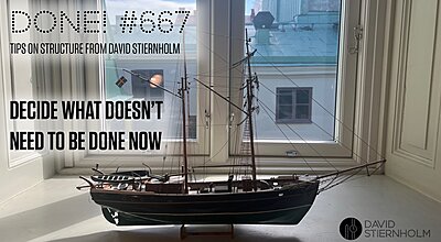 A detailed model sailing ship stands on a windowsill in front of a large window overlooking rooftops and a blue sky.