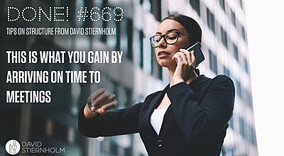 A businesswoman standing outside office buildings talks on her phone while checking the time on her wristwatch.
