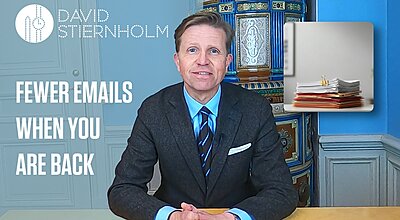 A man in a suit sits at a desk in a video frame with the text “FEWER EMAILS WHEN YOU ARE BACK” beside him and an image of a stack of documents.