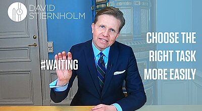 A man in a suit gestures while speaking in a video with the text “#WAITING” and “CHOOSE THE RIGHT TASK MORE EASILY” displayed beside him.