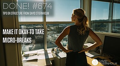 A woman stands in an office with her hands on her hips, looking out over a sunlit city through large windows.