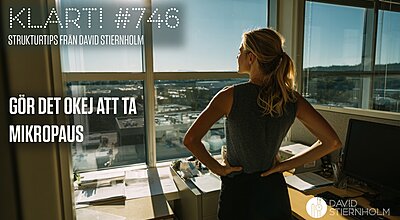 En kvinna står på ett kontor med händerna i sidan och blickar ut över en solbelyst stad genom stora fönster.