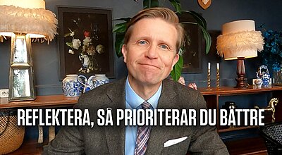 En man i grå kavaj och blå skjorta sitter i ett dekorerat rum med den svenska texten "REFLEKTERA, SÅ PRIORITERAR DU BÄTTRE" visad längst ner i bilden.